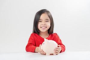 liten asiatisk flicka som sparar pengar i en spargris, lär sig att spara, barn sparar pengar för framtida utbildning. pengar, ekonomi, försäkring och människor koncept foto