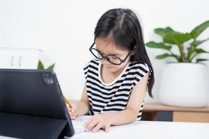 asiatisk barn flicka studerande Wow upphetsad på video ring upp inlärning till studerar uppkopplad klass eller person lära sig från Hem skola med läsplatta foto