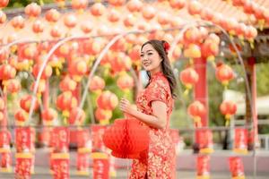 Lycklig asiatisk kvinna bär traditionell Cheongsam qipao klänning innehav lykta medan besöker de kinesisk buddist tempel. kinesisk ny år begrepp foto