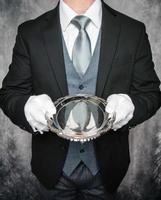 porträtt av formell butler eller servitör i mörk kostym och vit handskar innehav silver- tjänande bricka. begrepp av service industri och professionell gästfrihet. foto