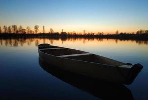 trä- båt på en stor skön sjö på solnedgång. foto