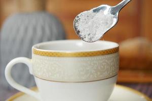 häller vit socker i en kaffe kopp foto