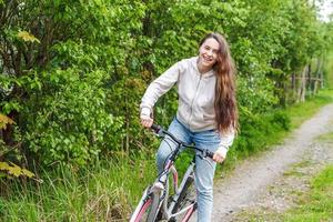 ung kvinna ridning cykel i sommar stad parkera utomhus. aktiva människor. hipster flicka koppla av och ryttare cykel foto