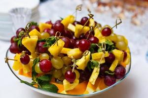 blandad färsk frukt på tallrik äpple vindruvor kiwi ananas grapefrukt orange banan och mynta foto