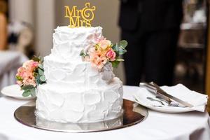 en mång nivå vit bröllop kaka på en silver- bas och rosa blommor på topp foto