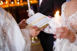 de präst sätta en ringa på brudgummens finger under traditionell bröllop i kyrka foto