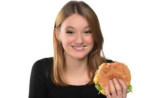 porträtt av en skön rolig ung flicka på de vit bakgrund, blond äter hamburgare. isolerat foto