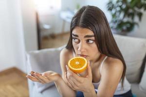 sjuk kvinna påfrestande till känsla lukt av halv färsk orange, har symptom av covid19, korona virus infektion - förlust av lukt och smak. ett av de huvud tecken av de sjukdom. foto