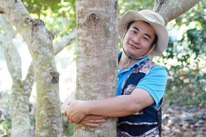 stilig asiatisk man botaniker kramar trunk av träd i skog. begrepp, kärlek natur och skydda, skog ,ekologi och miljö bevarande. . foto