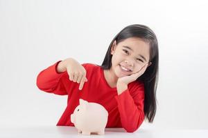liten asiatisk flicka som sparar pengar i en spargris, lär sig att spara, barn sparar pengar för framtida utbildning. pengar, ekonomi, försäkring och människor koncept foto