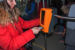 ung eleganta kvinna använder sig av en biljett stansning maskin i offentlig transport. de flicka slag de biljett. foto