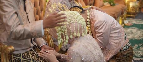de brud och brudgum knäböja på henne föräldrar knä under de bröllop ceremoni i en traditionell bröllop ceremoni i indonesien foto