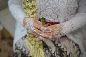 skön brud innehav betel blad medan bär bröllop klänning med jasmin och magnolia blomma halsband för en traditionell bröllop ceremoni i indonesien foto