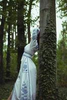 stänga upp kvinna i broderad klänning lutande mot träd trunk begrepp Foto