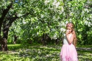 förtjusande liten flicka i blomstrande äpple fruktträdgård på solig dag foto