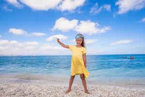 Lycklig liten flicka med papper flygplan under strand semester foto