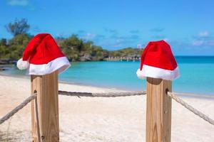närbild två santa hattar på staket på tropisk vit strand foto