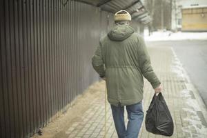 gammal man promenader med väska av specerier. pensionär i Ryssland. man promenader ner gata. foto