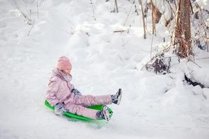 förtjusande liten Lycklig flicka sledding i vinter- snöig dag. foto