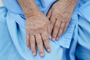 asiatisk äldre äldre kvinna patient sitter på sängen på sjukhus, närbild på hennes hand. foto