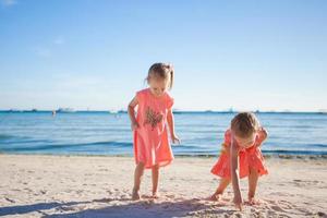 två liten systrar spelar tillsammans på de vit strand foto