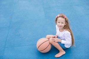 liten flicka med basketboll på de utomhus- domstol på tropisk tillflykt foto