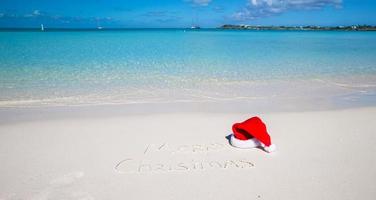 santa hatt på vit sandig strand och glad jul skriven i de sand foto