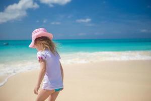 förtjusande liten flicka spelar i grund vatten på perfekt strand foto