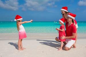 familj i santa hattar har roligt på tropisk strand foto