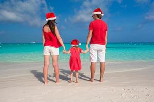 Lycklig familj i santa hattar har roligt på vit strand foto