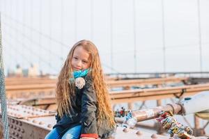 förtjusande liten flicka Sammanträde på brooklyn bro i ny york foto