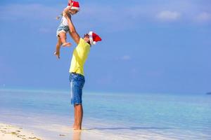 liten flicka och Lycklig pappa i santa hatt under strand semester foto