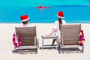 ung par i santa hattar avkopplande på strand under jul semester foto