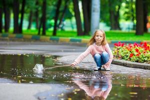 liten Lycklig flicka har roligt i en stor pöl i höst parkera foto