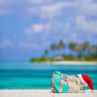 strand väska, baddräkt, Solskydd flaska och santa hatt på vit tropisk strand foto