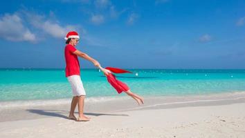 liten flicka och Lycklig pappa i santa hatt ha roligt på tropisk strand foto