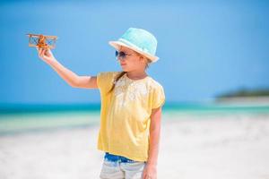 Lycklig barn flicka spelar med leksak flygplan på de strand. unge dröm av passande en pilot foto