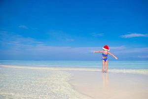 liten Lycklig flicka i santa hatt under strand semester på maldiverna foto