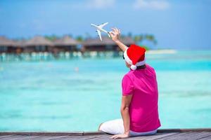 ung man i santa hatt på vit strand med miniatyr- av flygplan foto