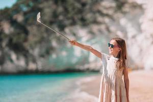 liten flicka tar selfie förbi henne smartphone på de strand. unge njuter henne suumer semester och framställning foton för minne