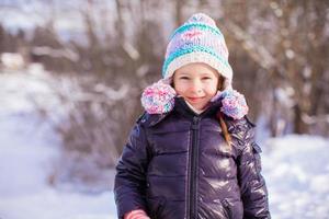 porträtt av liten förtjusande flicka i vinter- hatt på snöig skog foto