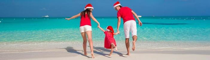 Lycklig familj i jul hattar har roligt på vit strand foto