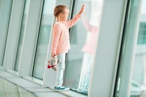 förtjusande liten flicka i flygplats med henne bagage väntar för ombordstigning foto