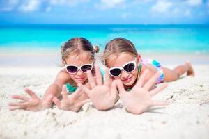liten flickor har roligt på tropisk strand spelar tillsammans på grund vatten. förtjusande liten systrar på strand under sommar semester foto