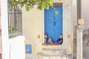 två liten förtjusande flickor Sammanträde på tröskel av gammal hus i emporio by, santorini, grekland foto