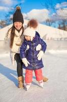 Lycklig upphetsad liten flicka och henne ung mor inlärning skridskoåkning foto