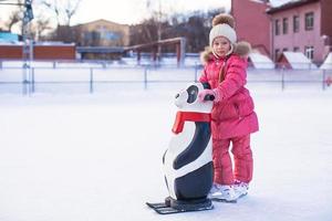 liten Lycklig flicka inlärning till skridsko på de rink foto