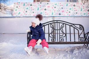 liten flicka Sammanträde på en bänk i de skridskoåkning rink foto