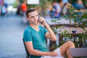 caucasian pojke är innehav mobiltelefon utomhus på de gata. man använder sig av mobil smartphone. foto