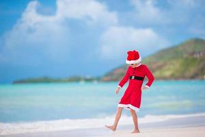 bedårande liten flicka i santa hatt på tropisk strand foto